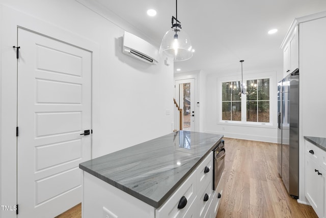 kitchen with white cabinets, an AC wall unit, hanging light fixtures, light wood-type flooring, and a center island