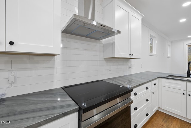 kitchen with wood finished floors, a sink, stainless steel electric stove, wall chimney range hood, and backsplash