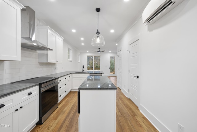 kitchen with a wall unit AC, stainless steel electric stove, white cabinetry, wall chimney range hood, and a center island