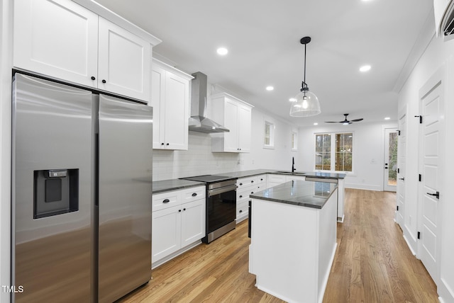 kitchen with stainless steel appliances, a peninsula, a sink, white cabinetry, and wall chimney exhaust hood