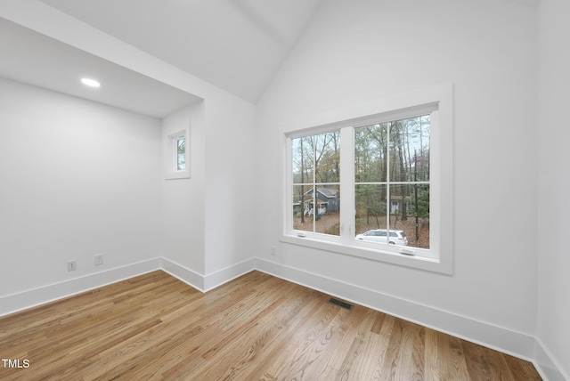 empty room featuring vaulted ceiling, light wood finished floors, visible vents, and baseboards