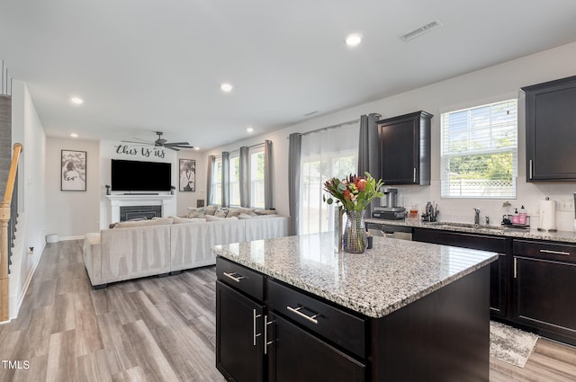 kitchen featuring light stone counters, ceiling fan, backsplash, light hardwood / wood-style flooring, and a center island