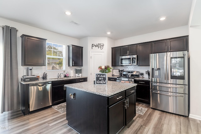 kitchen with a kitchen island, appliances with stainless steel finishes, light wood-type flooring, sink, and light stone counters