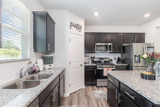 kitchen featuring appliances with stainless steel finishes, light hardwood / wood-style flooring, light stone countertops, and sink