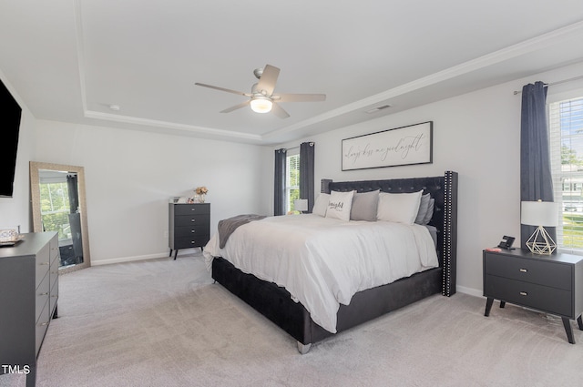 bedroom with a raised ceiling, light colored carpet, and ceiling fan