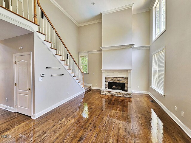 unfurnished living room with crown molding, hardwood / wood-style floors, a high ceiling, and a stone fireplace