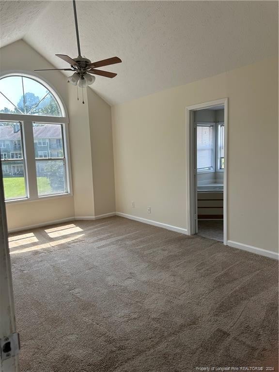 carpeted spare room featuring vaulted ceiling, a textured ceiling, and ceiling fan