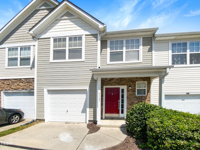 townhome / multi-family property with an attached garage, stone siding, and concrete driveway