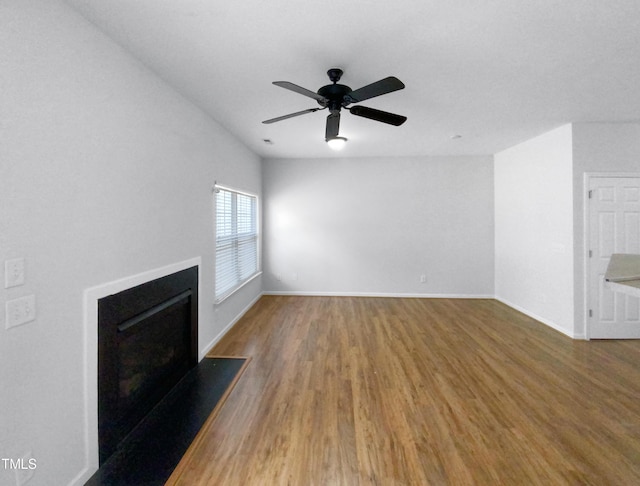 unfurnished living room featuring ceiling fan, a fireplace, baseboards, and wood finished floors