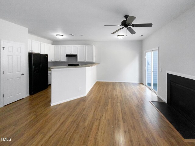 kitchen with a fireplace with raised hearth, dark wood-style floors, freestanding refrigerator, a peninsula, and white cabinetry