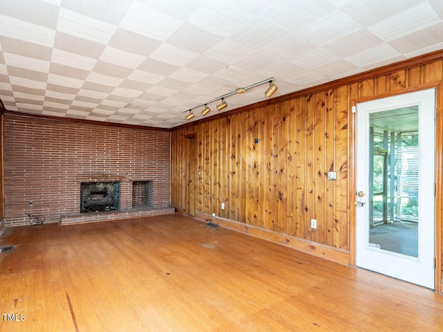 unfurnished living room featuring wood walls, track lighting, light hardwood / wood-style flooring, and a fireplace