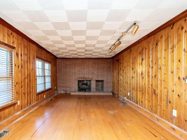 unfurnished living room featuring wood walls, wood-type flooring, a fireplace, rail lighting, and ornamental molding