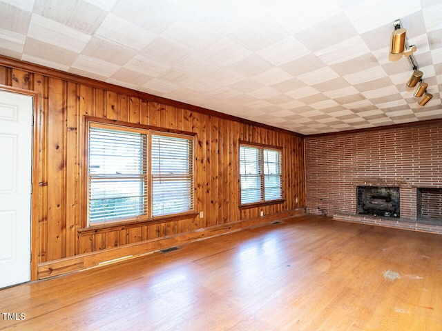 unfurnished living room featuring wood walls, wood-type flooring, and a brick fireplace