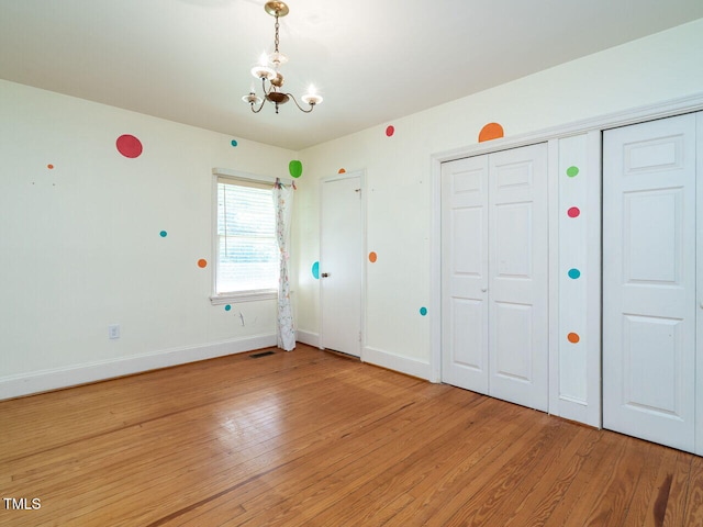 unfurnished bedroom featuring an inviting chandelier and hardwood / wood-style floors