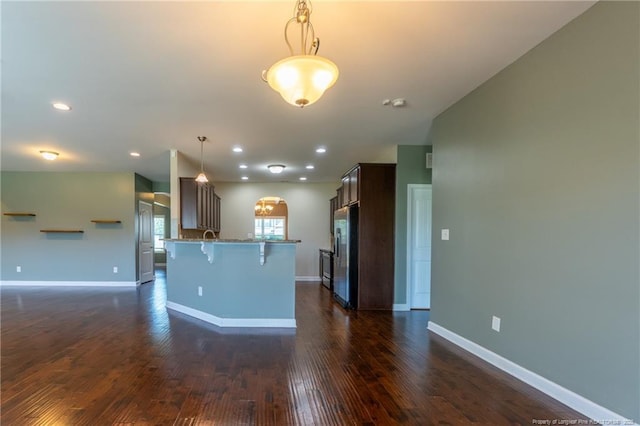 kitchen with pendant lighting, a breakfast bar area, stainless steel fridge, dark hardwood / wood-style flooring, and dark brown cabinetry