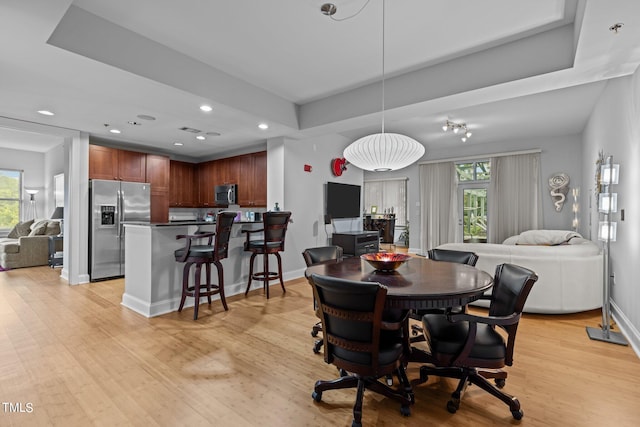 dining area featuring a tray ceiling, light hardwood / wood-style floors, and a healthy amount of sunlight