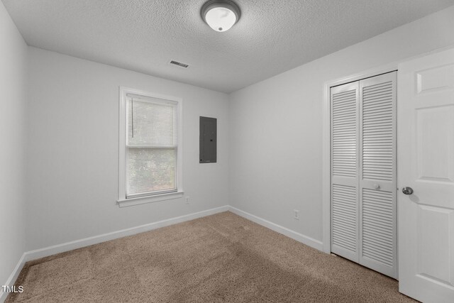 unfurnished bedroom with carpet, a textured ceiling, electric panel, and a closet