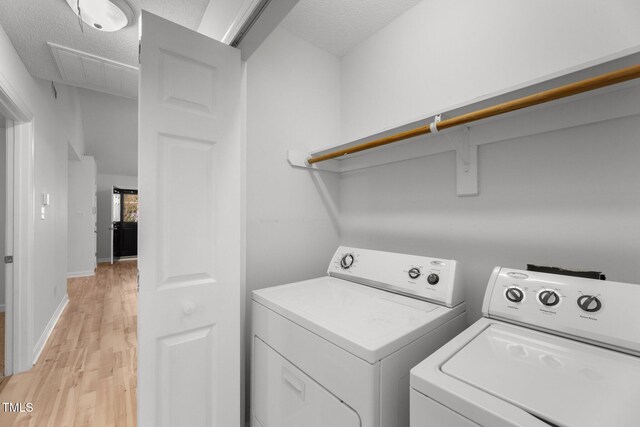 clothes washing area with washing machine and clothes dryer, light hardwood / wood-style flooring, and a textured ceiling