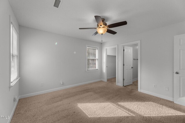 unfurnished bedroom featuring ceiling fan, light colored carpet, a spacious closet, and a textured ceiling