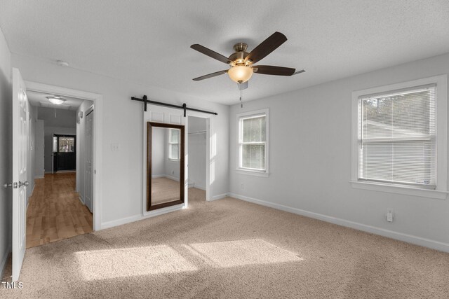 unfurnished bedroom featuring ceiling fan, a barn door, carpet floors, and a closet