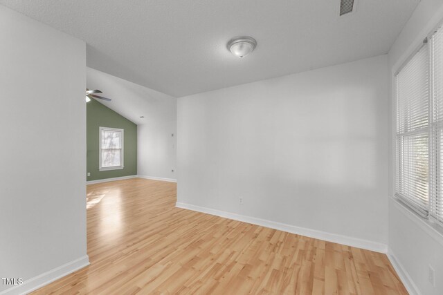 unfurnished room featuring light hardwood / wood-style floors, a textured ceiling, and vaulted ceiling