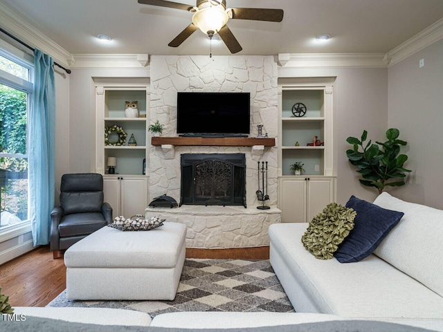 living room featuring ornamental molding, ceiling fan, hardwood / wood-style floors, and a stone fireplace