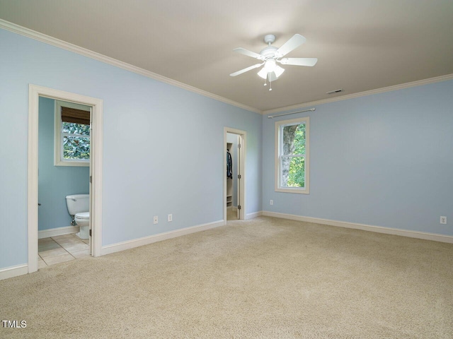 unfurnished bedroom with light carpet, crown molding, ceiling fan, a spacious closet, and ensuite bathroom