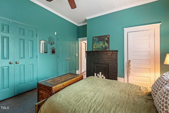 bedroom featuring dark hardwood / wood-style floors, a brick fireplace, crown molding, two closets, and ceiling fan