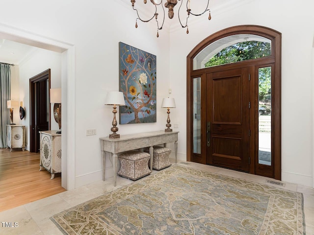 foyer featuring baseboards, ornamental molding, visible vents, and a chandelier