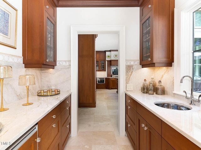 kitchen with light stone counters, backsplash, a sink, brown cabinets, and glass insert cabinets