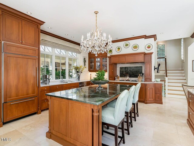 kitchen with paneled fridge, pendant lighting, a center island, ornamental molding, and dark stone countertops