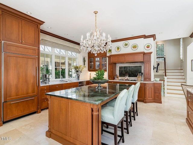 kitchen featuring a kitchen breakfast bar, a center island, a notable chandelier, brown cabinetry, and paneled refrigerator