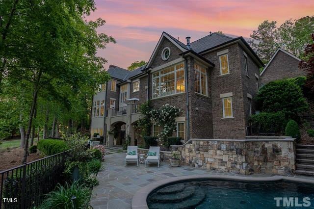 back house at dusk with a fenced in pool and a patio area