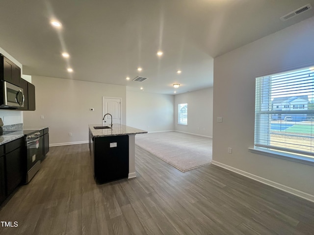 kitchen with dark wood-type flooring, sink, an island with sink, light stone counters, and stainless steel appliances