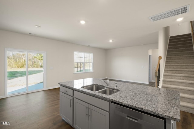 kitchen with light stone counters, dark hardwood / wood-style flooring, an island with sink, stainless steel dishwasher, and sink