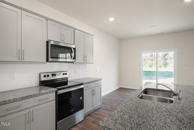 kitchen with dark wood-type flooring, dark stone countertops, appliances with stainless steel finishes, and sink