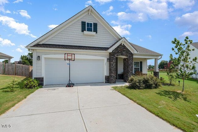 craftsman-style house featuring driveway, stone siding, fence, and a front yard