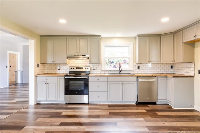 kitchen featuring backsplash, appliances with stainless steel finishes, a sink, wood finished floors, and under cabinet range hood