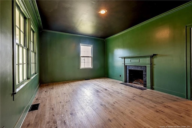 unfurnished living room with wood-type flooring, a fireplace, crown molding, and visible vents