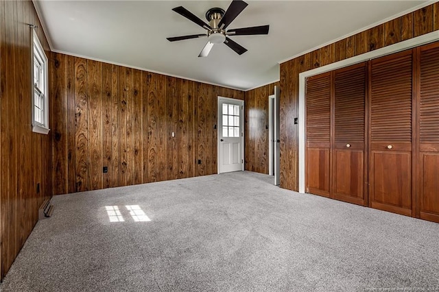 unfurnished bedroom featuring ornamental molding, a closet, carpet flooring, and wood walls