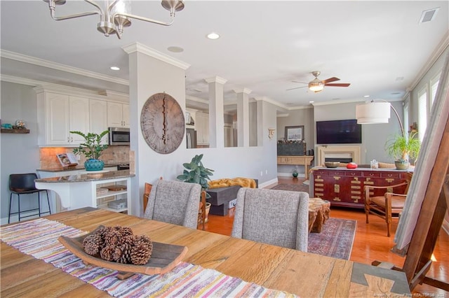 dining space featuring light wood-type flooring, ceiling fan with notable chandelier, and ornamental molding