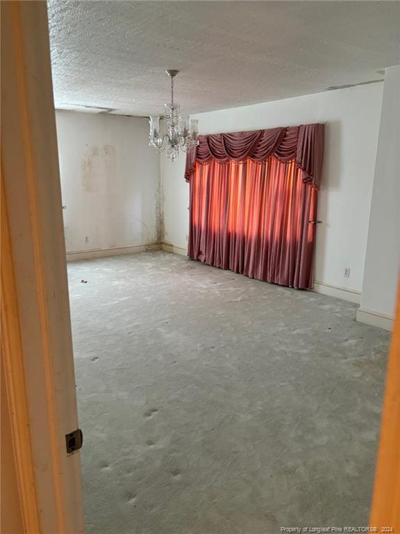 empty room with a textured ceiling, concrete floors, and a notable chandelier