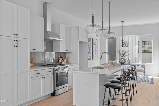 kitchen featuring gas range, a kitchen island with sink, white cabinets, and wall chimney range hood