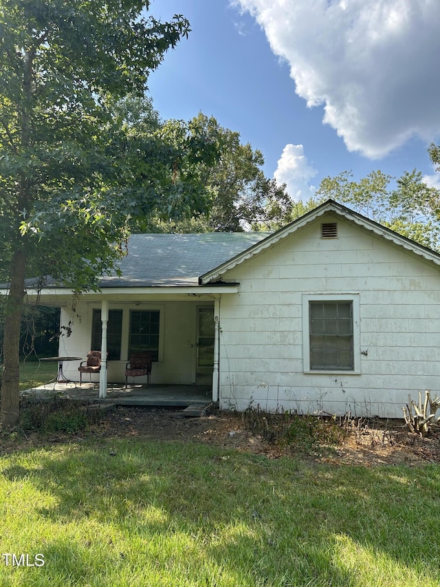 rear view of property with a lawn, roof with shingles, and covered porch