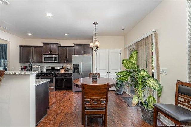 kitchen featuring light stone countertops, appliances with stainless steel finishes, dark hardwood / wood-style flooring, pendant lighting, and dark brown cabinetry