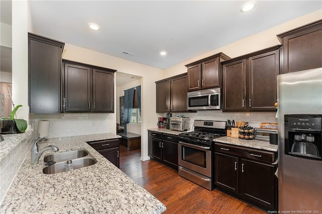 kitchen featuring light stone counters, dark wood-style floors, a sink, dark brown cabinetry, and appliances with stainless steel finishes