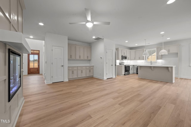 kitchen featuring a breakfast bar, stainless steel appliances, a kitchen island, decorative light fixtures, and light wood-type flooring