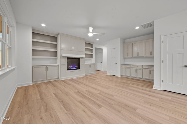 unfurnished living room featuring ceiling fan, a large fireplace, and light wood-type flooring