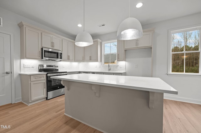 kitchen featuring decorative light fixtures, light hardwood / wood-style flooring, a wealth of natural light, stainless steel appliances, and decorative backsplash