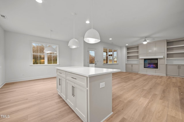 kitchen with a center island, hanging light fixtures, ceiling fan, light hardwood / wood-style floors, and white cabinets